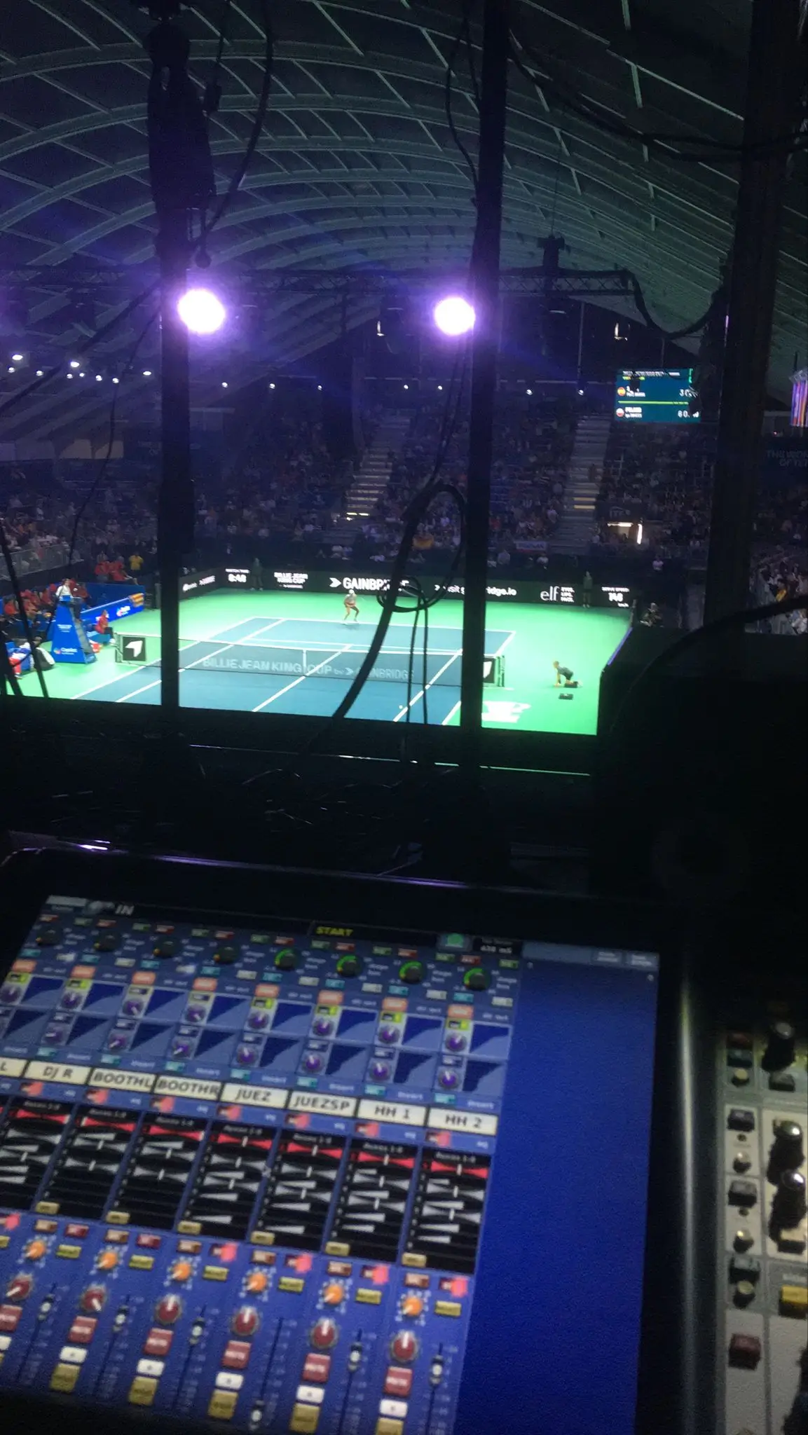 Mesa de som em primeiro plano e a quadra de tênis durante uma partida da Billie Jean King Cup 2024 em Málaga.