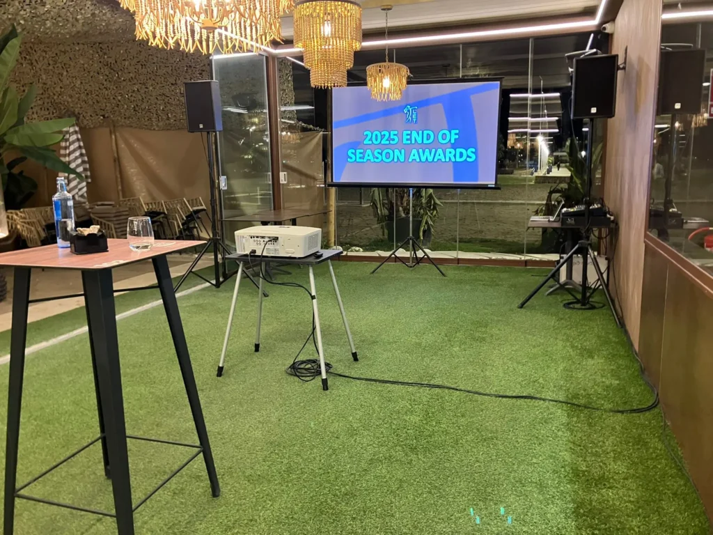A large screen displaying the 2025 End of Season Awards program alongside a portable projector and sound equipment.