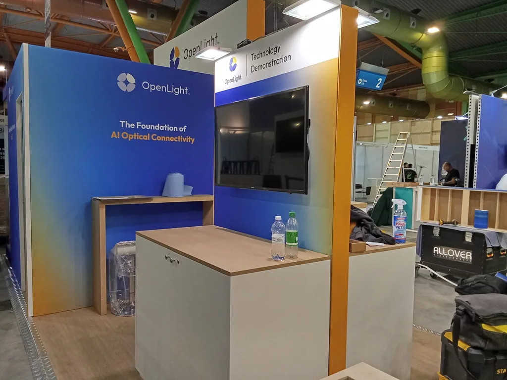 A screen mounted under a technology demonstration header on an exhibitor stand at ECOC 2026, with protective wrapping still on the furniture.