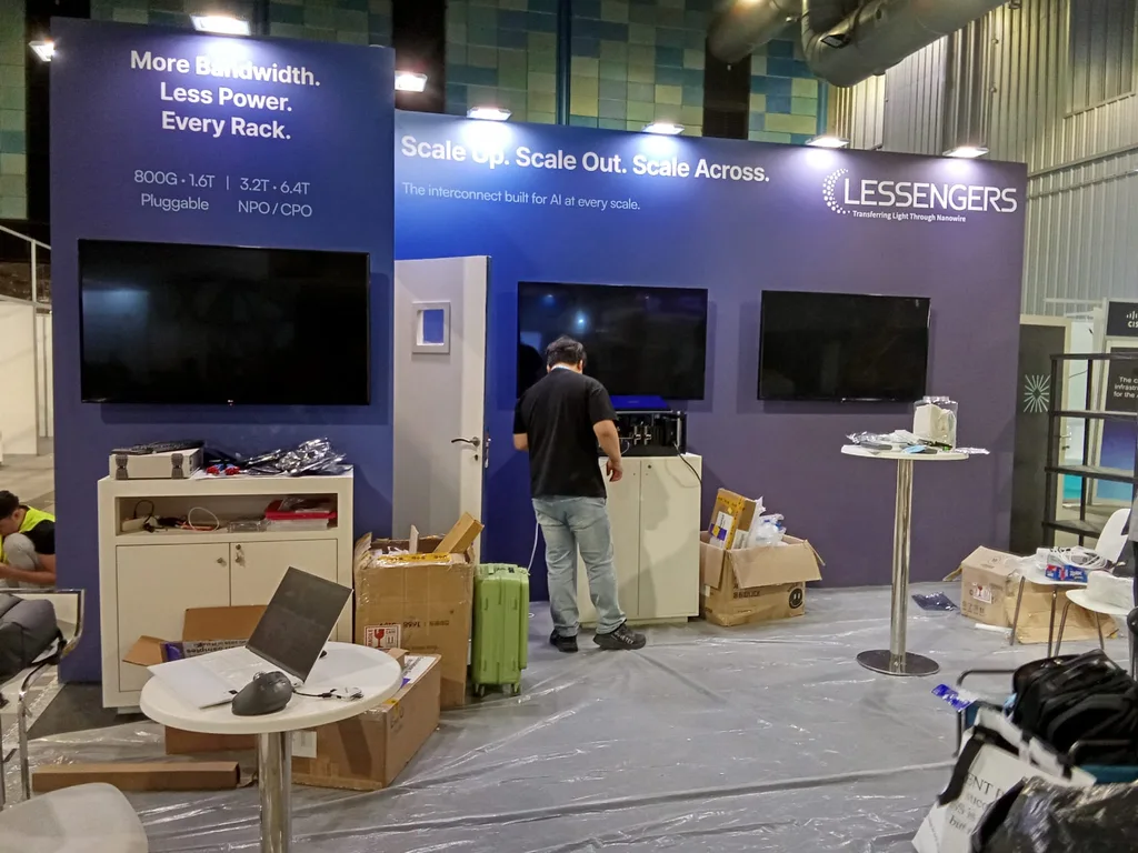 Three wall mounted screens on an exhibitor stand at ECOC 2026, with packing boxes and flight cases still on the floor during installation.