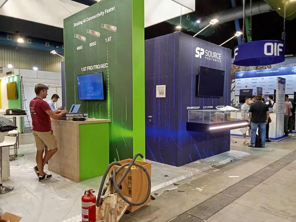 Screens installed on two neighbouring stands at the ECOC 2026 exhibition, with the aisle still covered in protective sheeting.