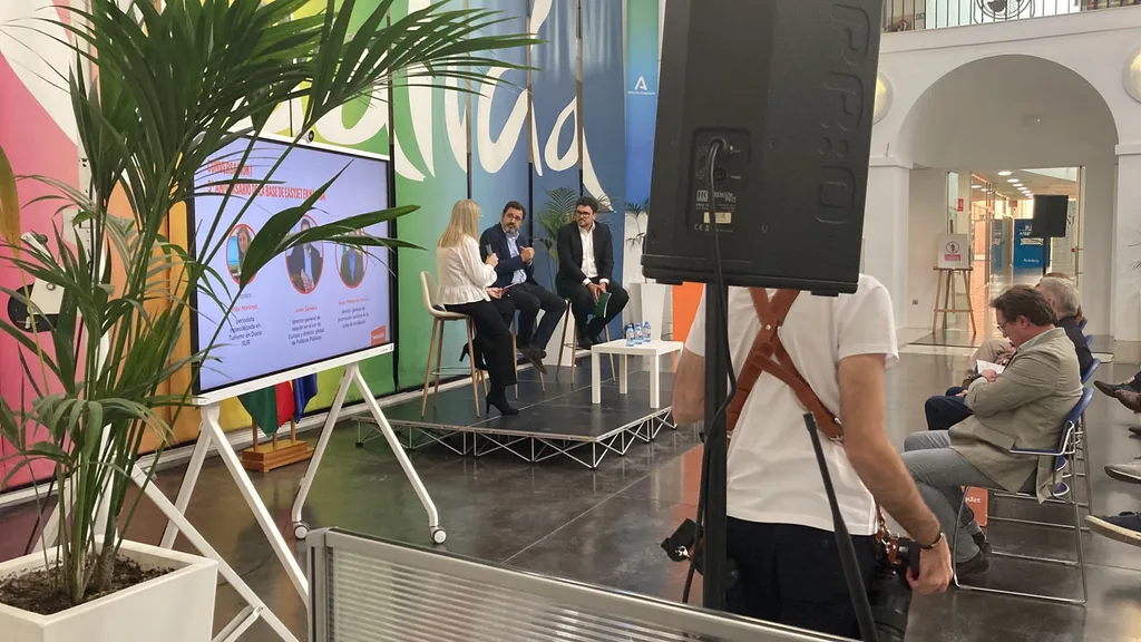 A talk in progress at the Tinkle event for easyJet in the centre of Malaga on 22 October 2026, with our sound system in the foreground. A talk in progress on a low stage at the Tinkle event for easyJet in the centre of Malaga, with a screen showing slides behind three seated speakers and a PA speaker on a stand in the foreground.